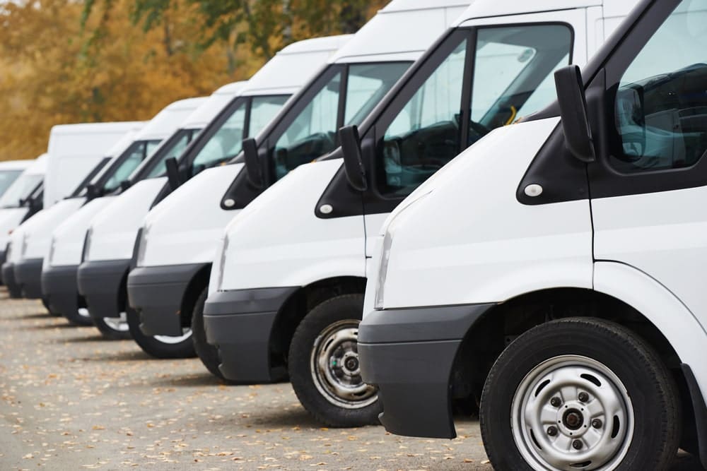 nine white vans parked in a row in a parking lot